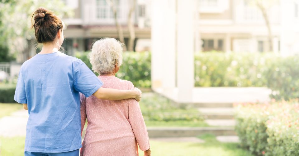 Oudere vrouw en verzorger wandelen samen, ondersteund door Fijnproevers' aangepaste voeding.